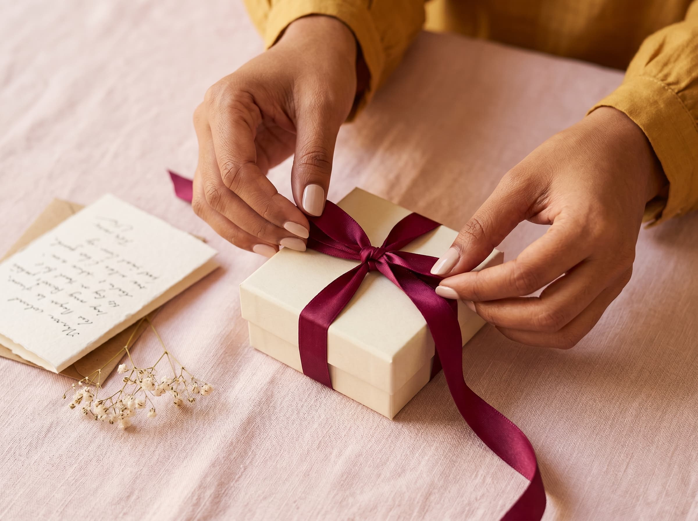 Hands tying a burgundy silk ribbon around an ivory jewellery box